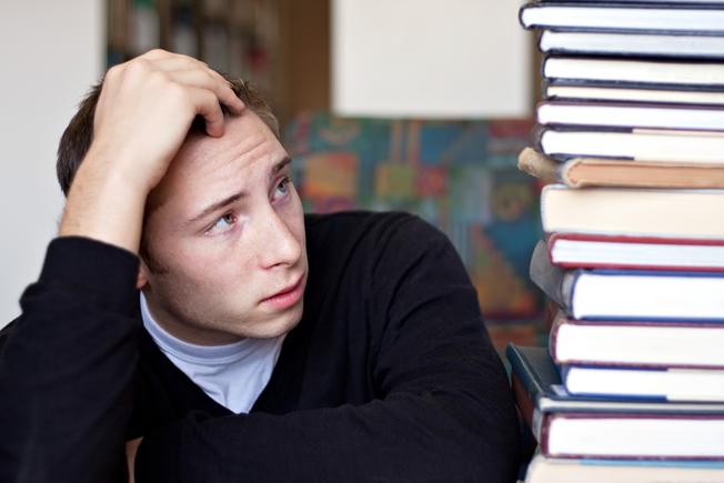 Desktop a frustrated and stressed out student looks up at the high pile of textbooks he has to go through to do his homework sttlftcsj